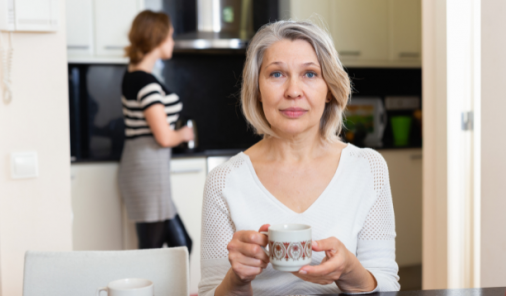 Mother in kitchen sitting at table with daughter in the background